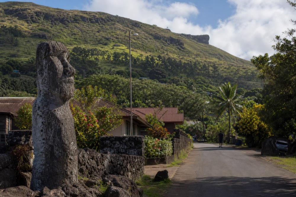 Street of low houses and flowering shrubs in Hanga Roa with a wooded hillside rising behind the rooftops