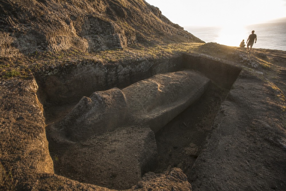 Unfinished moai lying on its back still attached to the volcanic bedrock inside a cut quarry niche