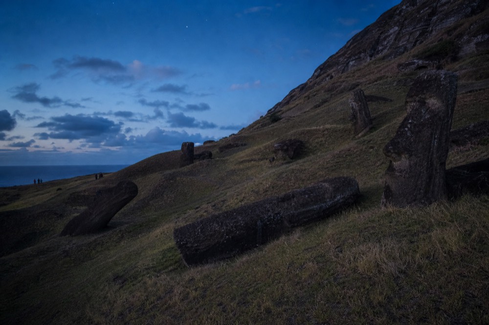 Half-carved moai lying at angles across the grassy inner slope of the Rano Raraku quarry under high summer light