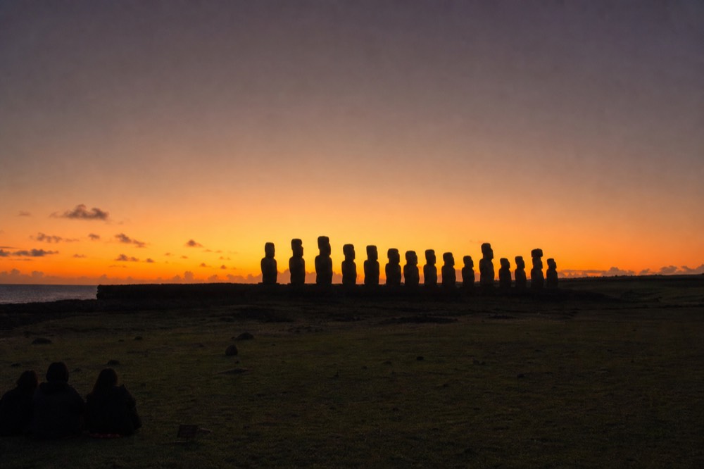 Silhouetted row of moai at Ahu Tongariki against a deep orange pre-dawn sky with the horizon still dark