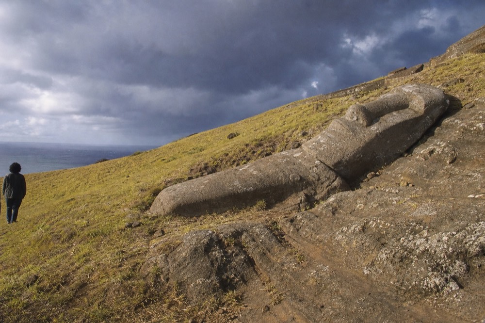 Unfinished moai lying on its back still attached to the bedrock high on the quarry slope