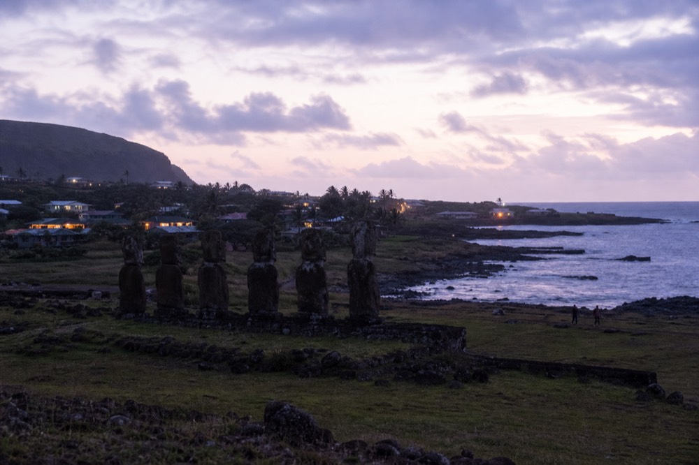 Low single-storey houses and gardens of Hanga Roa spread across a green slope down to a rocky shoreline